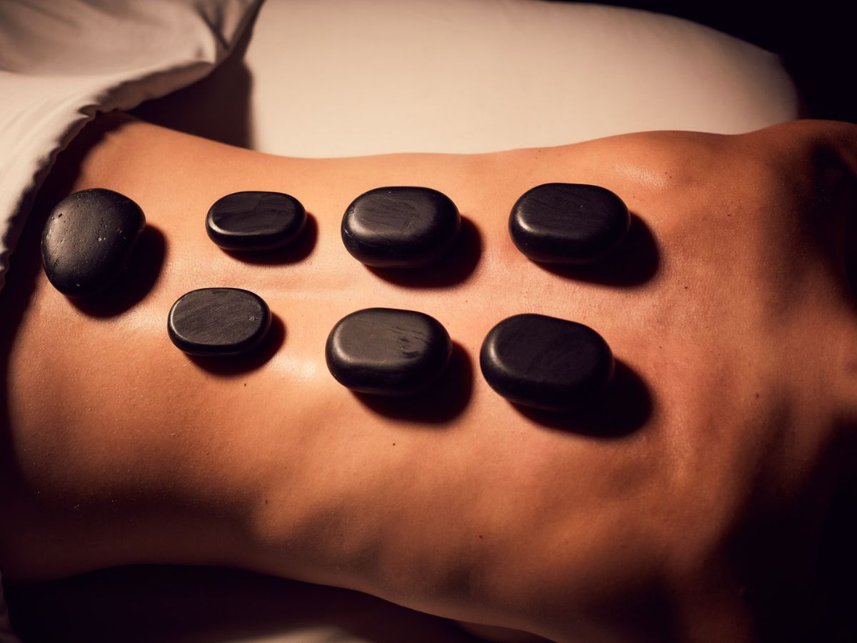 Woman with seven warm basalt stones on her back to help release tension during a massage at Viva Day Spa + Med Spa.